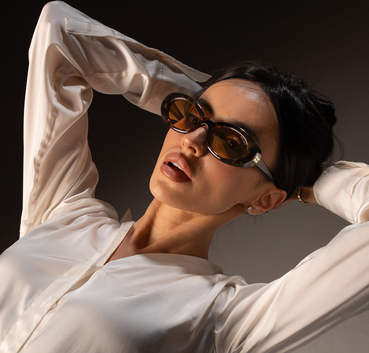 Woman wearing tortoiseshell Miu Miu sunglasses with amber lenses in bright sunlight, in a cream silk shirt